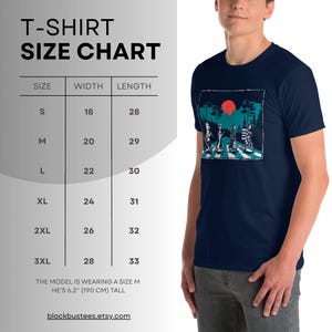 May include: Navy blue t-shirt featuring a graphic of a band crossing a street with a red sun. The shirt is displayed with a size chart showing measurements in inches. The model is wearing a size M and is 6'2" tall.
