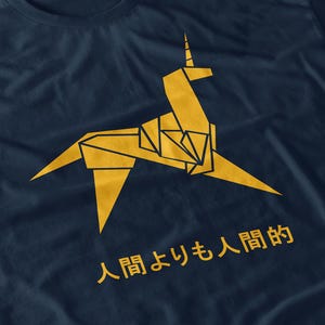 May include: Navy blue t-shirt with a gold origami unicorn design and Japanese text. The design is printed on a soft, comfortable fabric. A stylish and unique graphic tee.