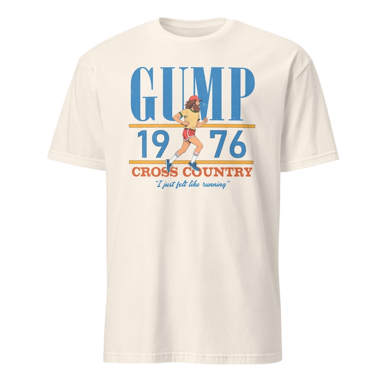 Puede incluir: Una camiseta color hueso con un gr&aacute;fico de un corredor con barba y gorra roja. El texto dice GUMP 1976 CROSS COUNTRY y I just felt like running en tinta azul, naranja y roja. El dise&ntilde;o incluye l&iacute;neas horizontales por encima y por debajo del a&ntilde;o.