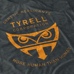 May include: Dark grey t-shirt with an orange graphic. The graphic features an owl-like design with the text "GENETIC REPLICANTS TYRELL CORPORATION MORE HUMAN THAN HUMAN."