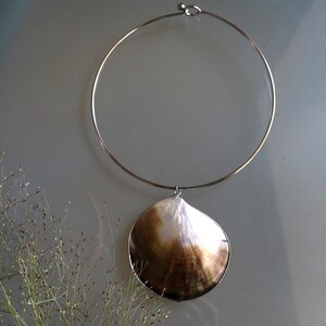 May include: A silver-toned metal choker necklace featuring a single, large, rounded seashell pendant. The shell displays a gradient of iridescent white and deep brown tones, suspended from a thin, circular wire band with a simple hook closure.