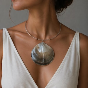 May include: A silver-toned metal choker necklace featuring a large, smooth, dark brown and grey seashell pendant. The shell has a natural, glossy finish with subtle color gradients, suspended from a thin, circular, rigid metal neck wire.