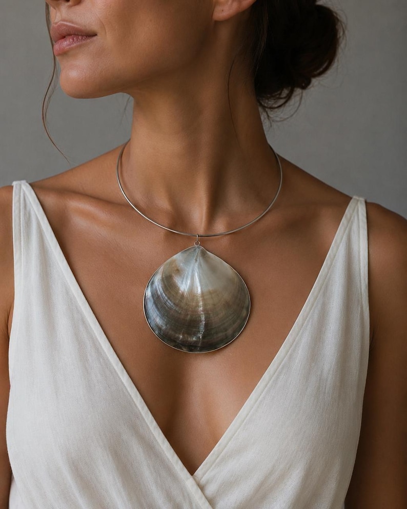May include: A silver-toned metal choker necklace featuring a large, smooth, dark brown and grey seashell pendant. The shell has a natural, glossy finish with subtle color gradients, suspended from a thin, circular, rigid metal neck wire.