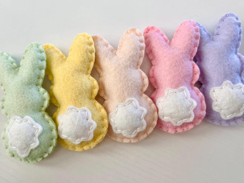 May include: Five felt Easter bunny decorations in different pastel colors: green, yellow, peach, pink, and purple. Each bunny has a white felt star on its bottom and is sewn with white thread.