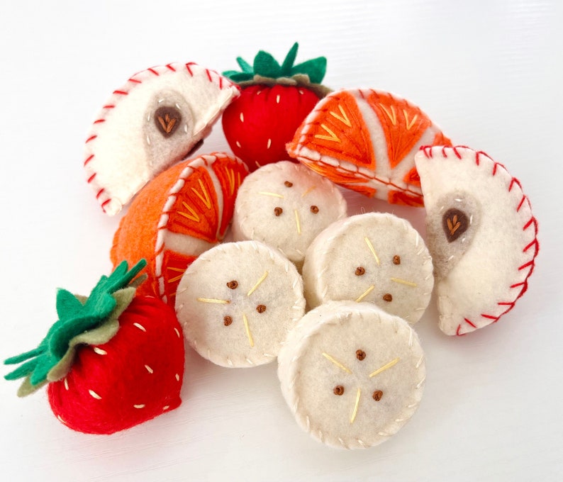 This set of felt fruit comes with four banana slices, two red apple slices, two orange slices, and two whole strawberries with two toned green leaves. Everything is completely hand stitched.