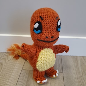 May include: A crocheted orange and yellow Pokemon character with blue eyes and a black mouth. The character has a long orange tail.