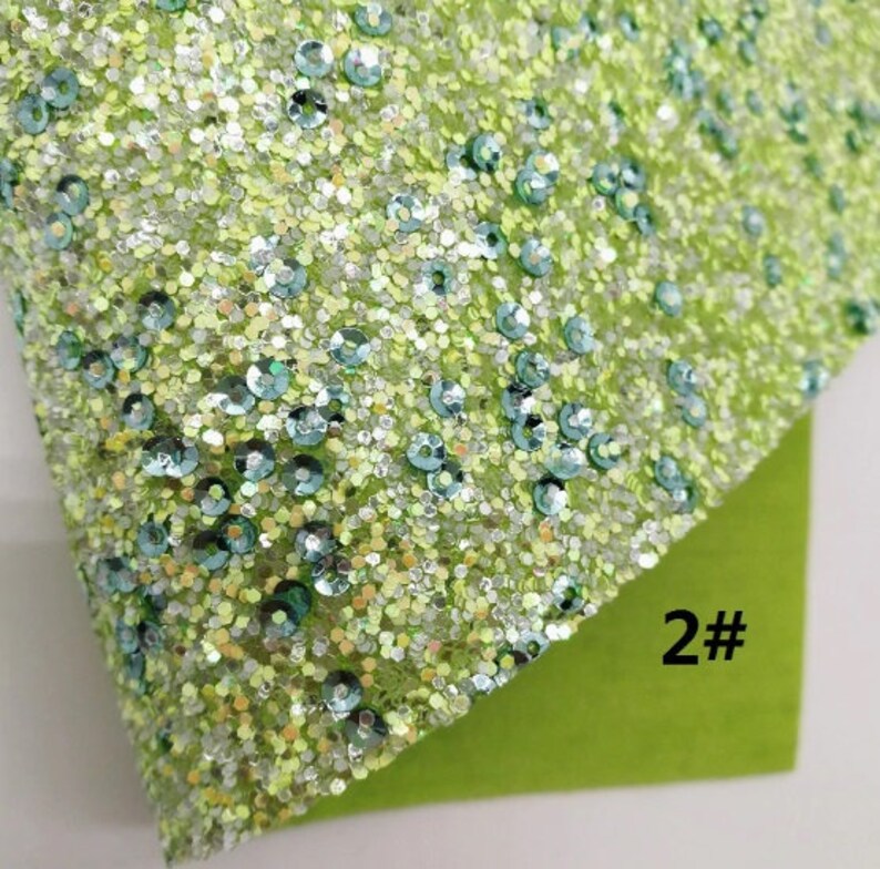 May include: Close-up of a sheet of lime green glitter fabric with iridescent sequins. The fabric is covered in small, sparkling glitter particles and larger, round sequins in shades of blue and green. The number "2#" is visible on a green backing.