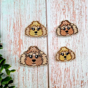 May include: Four embroidered felt patches of brown and blonde dogs with black eyes. The patches are on a light blue wooden background.