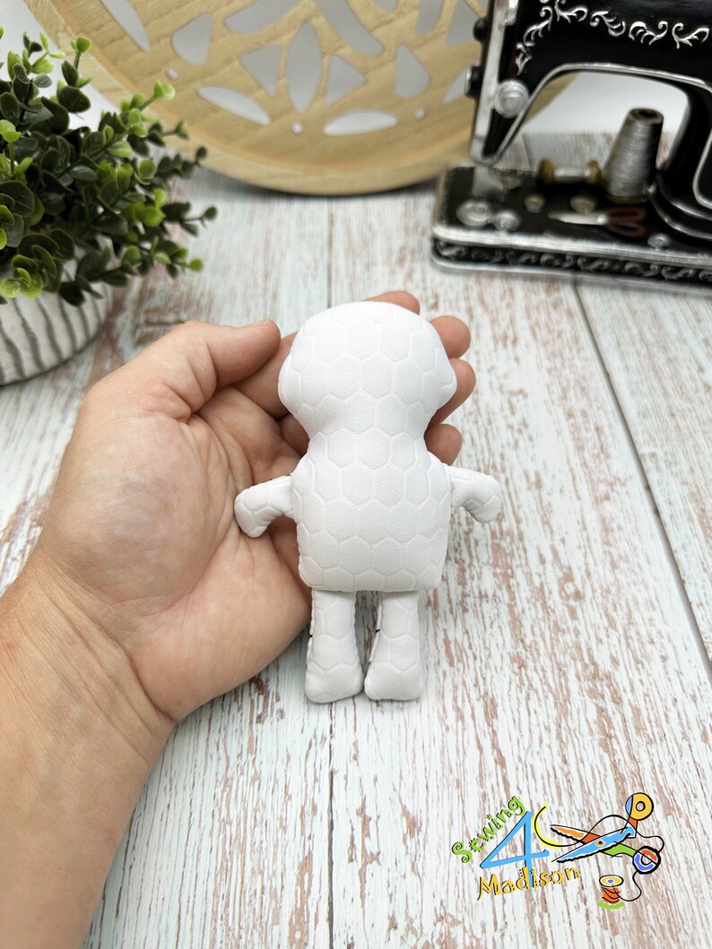 Puede incluir: Mu&ntilde;eca de tela blanca con un patr&oacute;n de panal. La mu&ntilde;eca tiene una cabeza redonda, dos brazos, dos piernas y un cuerpo peque&ntilde;o. La mu&ntilde;eca est&aacute; sostenida en la mano de una persona.