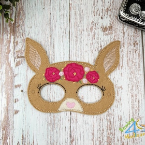 May include: A brown felt bunny mask with pink flower embroidery and black eyelashes. The mask has cutouts for the eyes.