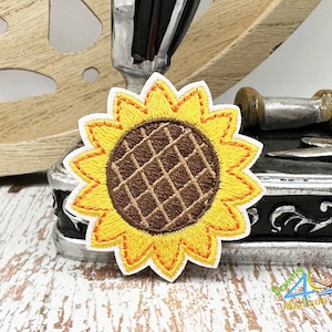 May include: A yellow and orange embroidered sunflower patch with a brown center. The sunflower is on a white background.