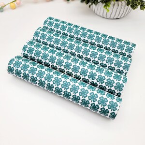 May include: Four rolls of white fabric with a repeating pattern of green four-leaf clovers. The clovers have the letters "H" inside each leaf. The fabric is rolled up and stacked on top of each other.