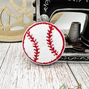 May include: A white felt baseball with red stitching, sitting on a wooden surface. The baseball is a craft supply for sewing projects.