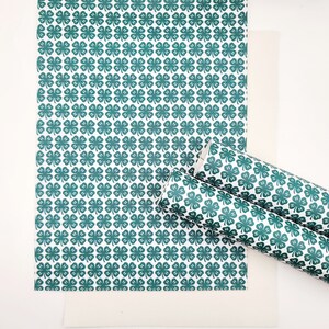 May include: White background with a sheet and a rolled piece of paper featuring a repeating pattern of green four-leaf clovers. The clover design is a dark teal color.