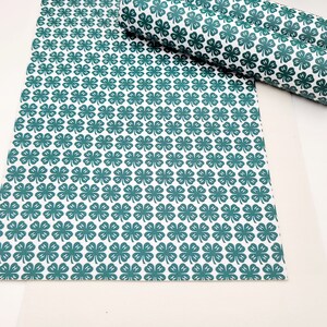 May include: White and teal clover patterned faux leather sheets, one flat and two rolled. The clover design is repeated across the surface. The material is suitable for crafting projects, such as making bows, earrings, or other accessories.