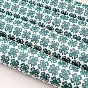 May include: Several rolls of white material with a repeating pattern of green four-leaf clovers, each with the letter "H" inside. The material is tightly rolled, and the pattern is visible on the surface.