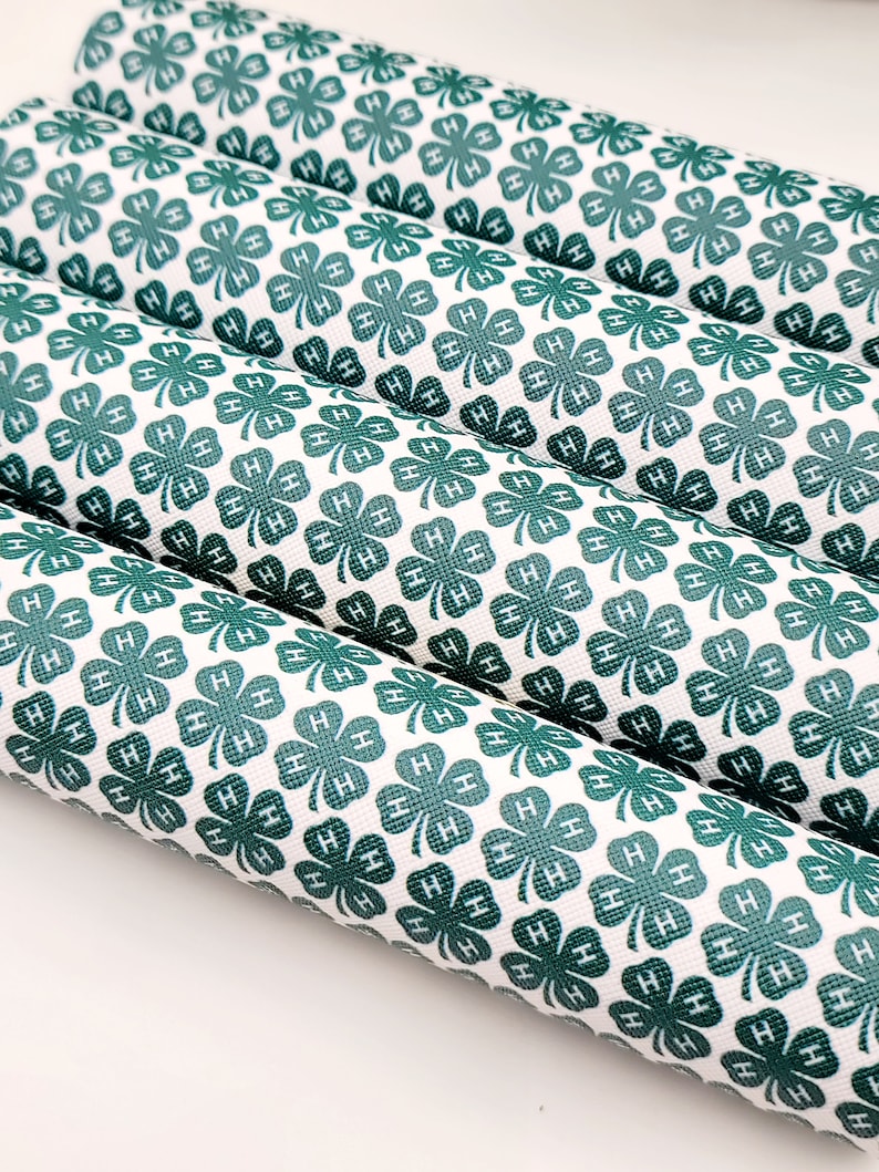 May include: Several rolls of white material with a repeating pattern of green four-leaf clovers, each with the letter "H" inside. The material is tightly rolled, and the pattern is visible on the surface.