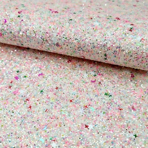 May include: A close-up of a sheet of pink and white glitter fabric. The fabric is covered in a variety of glitter shapes, including stars, moons, and circles, in shades of pink, green, and red. The fabric is folded over, showing the texture and depth of the glitter.