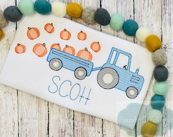 May include: A blue tractor with a trailer full of orange pumpkins. The tractor is pulling the trailer along a white surface. The text "SCOTT" is embroidered below the tractor.