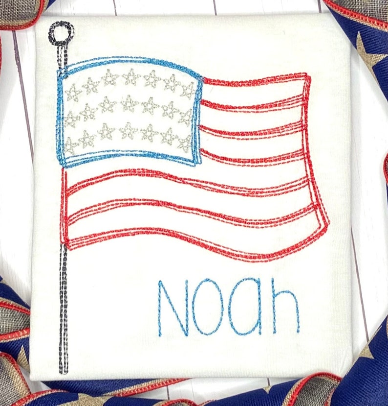 May include: A white t-shirt with an embroidered American flag and the name "Noah" in blue thread.