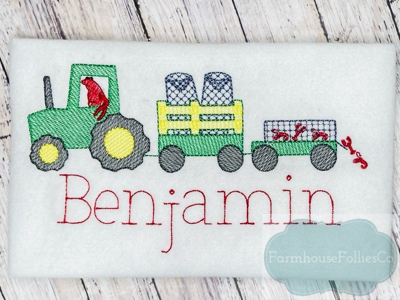 May include: Green tractor pulling a wagon with a red lobster and a name "Benjamin" embroidered on a white fabric.