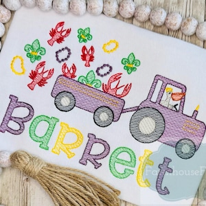 K&ouml;nnte beinhalten: Gestickte Darstellung eines lila Traktors, der einen Wagen voller Krebse zieht, mit einem Pelikan am Steuer. Der Wagen ist mit Mardi Gras-Perlen und Fleur-de-lis verziert. Der Name "Barrett" ist unter dem Traktor in bunten Buchstaben gestickt.