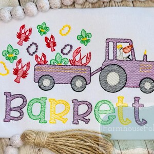 K&ouml;nnte beinhalten: Gestickte Darstellung eines lila Traktors, der einen Wagen voller Mardi Gras-Perlen und Krebse zieht. Der Name "Barrett" ist unter dem Traktor gestickt.