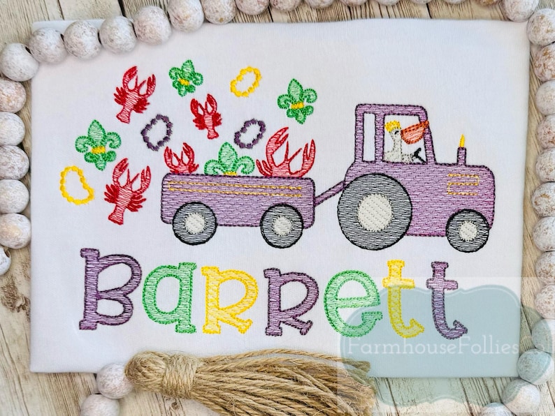 K&ouml;nnte beinhalten: Gestickte Darstellung eines lila Traktors, der einen Wagen voller Mardi Gras-Perlen und Krebse zieht. Der Name "Barrett" ist unter dem Traktor gestickt.