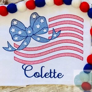 May include: Embroidered design of an American flag with a blue bow and white stars. The name Colette is embroidered below the flag.