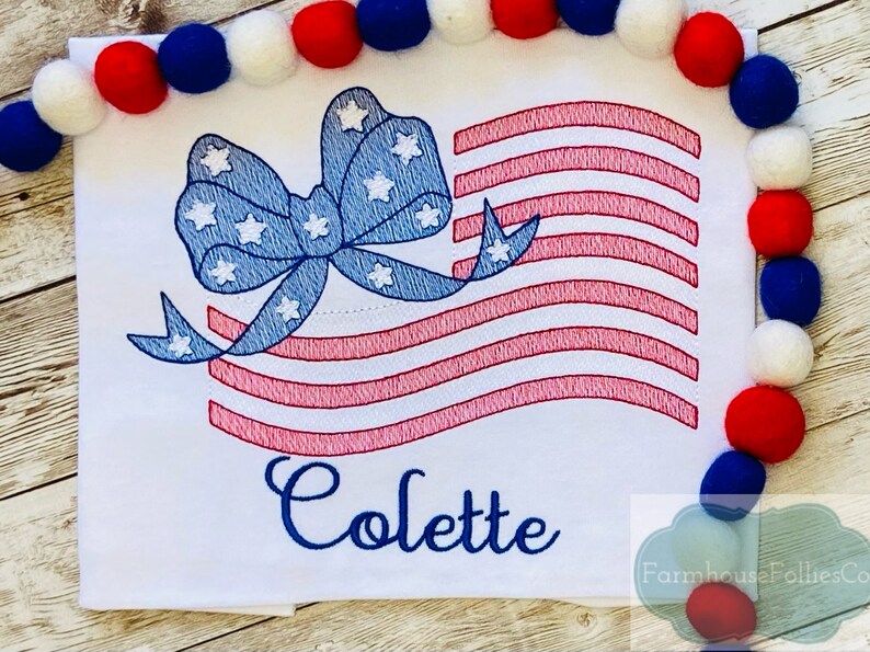 May include: Embroidered design of an American flag with a blue bow and white stars. The name Colette is embroidered below the flag.