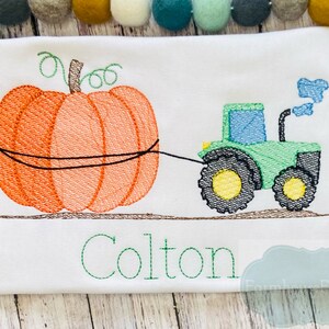 May include: Embroidered design of a green tractor pulling an orange pumpkin with the name Colton stitched below.