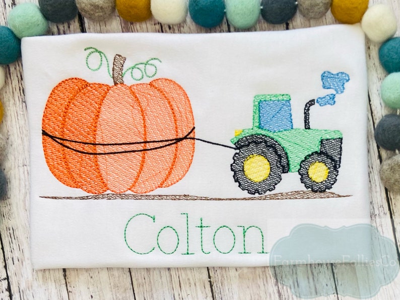 May include: Embroidered design of a green tractor pulling an orange pumpkin with the name Colton stitched below.