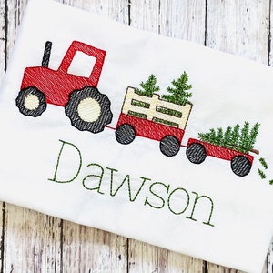 May include: Red toy tractor pulling a wagon with Christmas trees. The wagon is filled with green trees and the tractor has the name Dawson embroidered on the front.