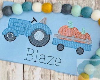 May include: A light blue shirt featuring a blue tractor pulling a wagon with two orange pumpkins. The name "Blaze" is embroidered below the tractor. A border of colorful felt balls surrounds the shirt.
