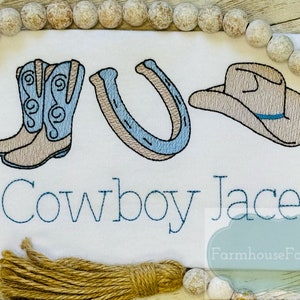 Puede incluir: Dise&ntilde;o bordado en una tela blanca con un par de botas de vaquero, una herradura, un sombrero de vaquero y el texto "Cowboy Jace".