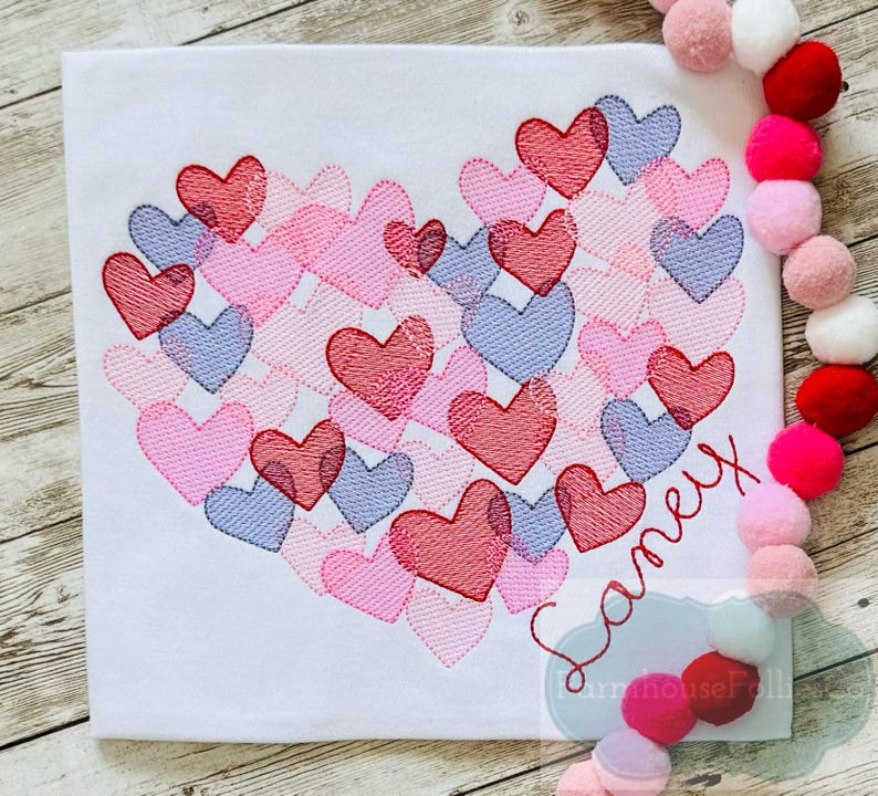 Pu&ograve; includere: Una maglietta bianca con un design a forma di cuore fatto di cuori rosa, rossi e viola. Il nome "Samey" &egrave; ricamato sotto il cuore.