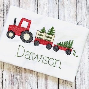 May include: Red toy tractor pulling a wagon full of Christmas trees with the name Dawson embroidered on a white shirt.
