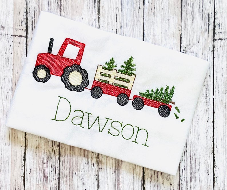May include: Red toy tractor pulling a wagon full of Christmas trees with the name Dawson embroidered on a white shirt.