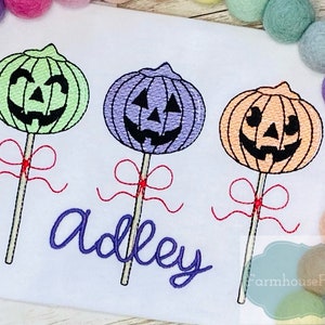 May include: Three embroidered pumpkin lollipops with red bows and sticks. The lollipops are green, purple, and orange. The word "adley" is embroidered in purple below the lollipops.