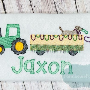 Puede incluir: Tractor verde tirando de un vag&oacute;n amarillo con un perro marr&oacute;n encima. El vag&oacute;n est&aacute; decorado con cuentas moradas y amarillas. El nombre Jaxon est&aacute; bordado debajo del tractor y el vag&oacute;n.