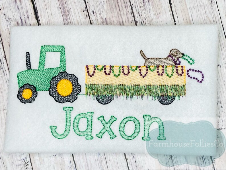 Puede incluir: Tractor verde tirando de un vag&oacute;n amarillo con un perro marr&oacute;n encima. El vag&oacute;n est&aacute; decorado con cuentas moradas y amarillas. El nombre Jaxon est&aacute; bordado debajo del tractor y el vag&oacute;n.