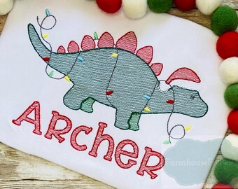 May include: Embroidered Christmas dinosaur design with red, green, and yellow lights. The dinosaur is wearing a Santa hat. The name "Archer" is embroidered below the dinosaur.