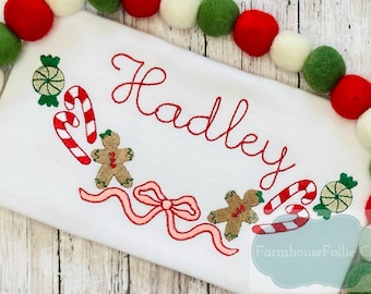 May include: White embroidered Christmas-themed baby onesie with the name "Hadley" in red thread. The design includes candy canes, gingerbread men, and a pink bow.