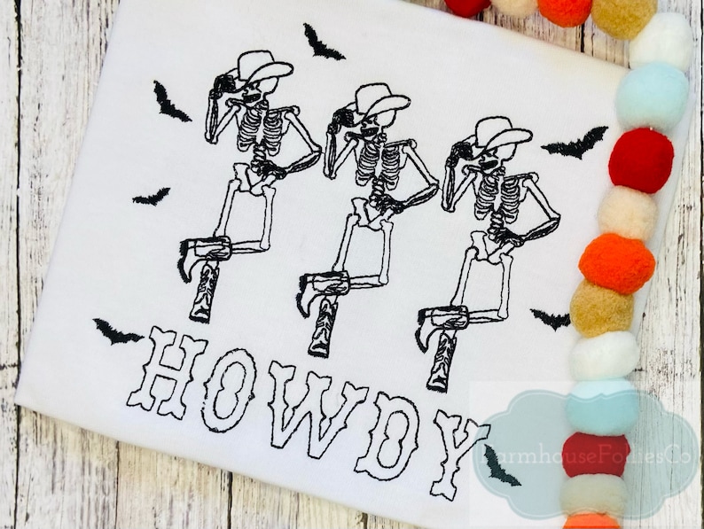 May include: White t-shirt with three black skeleton cowboys wearing hats and boots. The skeletons are in a line and are all facing the right. The word "HOWDY" is written in black below the skeletons. There are black bats flying around the skeletons.