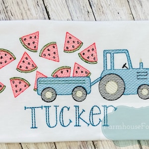 May include: A blue tractor with a wagon full of watermelon slices. The tractor is pulling a wagon full of watermelon slices. The word "TUCKER" is embroidered below the tractor.
