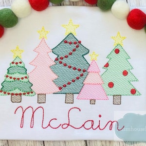 May include: Embroidered Christmas tree design with the name "McClain" in red thread. The design features five trees with different colors and decorations, including stars, lights, and ornaments.