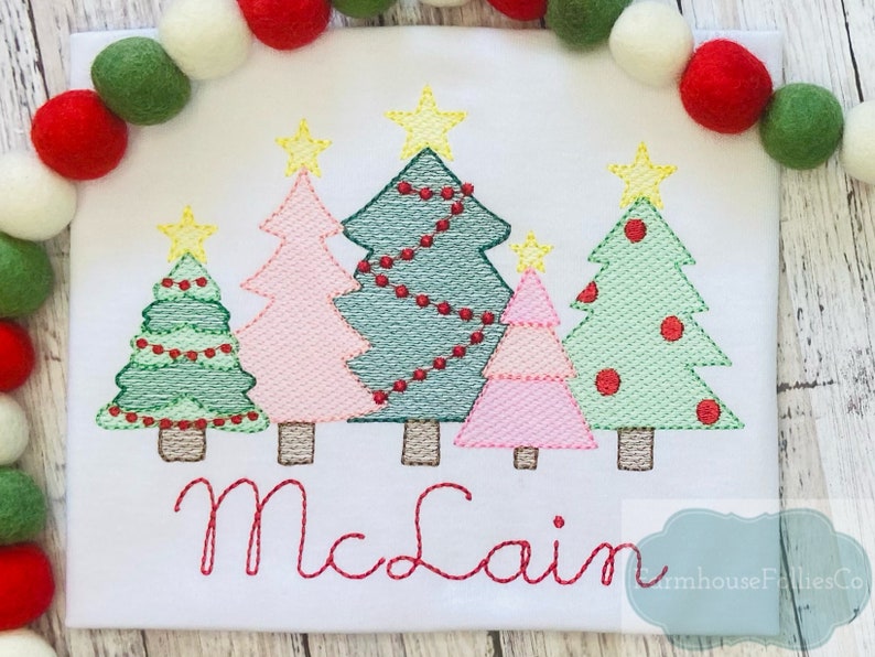 May include: Embroidered Christmas tree design with the name "McClain" in red thread. The design features five trees with different colors and decorations, including stars, lights, and ornaments.