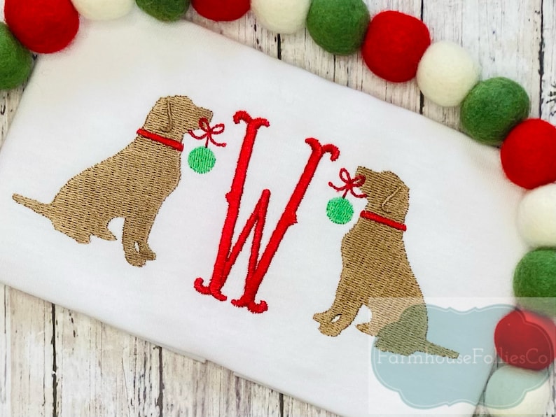 K&ouml;nnte beinhalten: Gestickte Darstellung von zwei braunen Hunden, die rote und gr&uuml;ne Weihnachtskugeln halten, mit einem roten Buchstaben W in der Mitte. Das Design ist auf einem wei&szlig;en Stoffhintergrund.