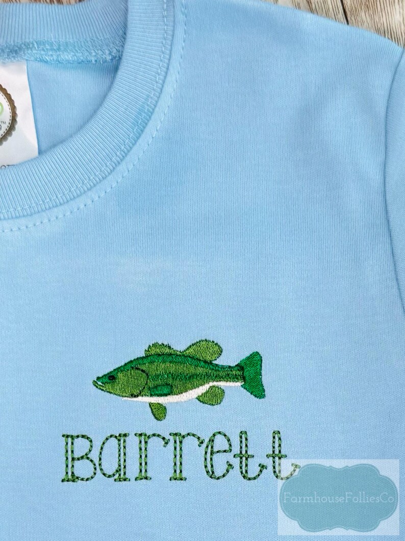 May include: Light blue long-sleeved shirt with an embroidered green fish design and the name "Barrett" in green thread. The shirt is made of a soft, comfortable material.
