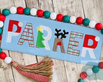 May include: A light blue rectangular Christmas-themed sign embroidered with the name "PARKER" in festive colors and patterns. The sign is surrounded by a garland of red, white, and teal wooden beads, with a tassel at the bottom.